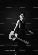 Young man holding acoustic guitar in dark studio