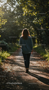 Woman walking alone on leafy forest path in sunlight