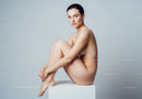 Nude woman sitting on white cube with knees hugged