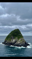 Lush Green Rocky Island with Cross Under Cloudy Sky over Ocean