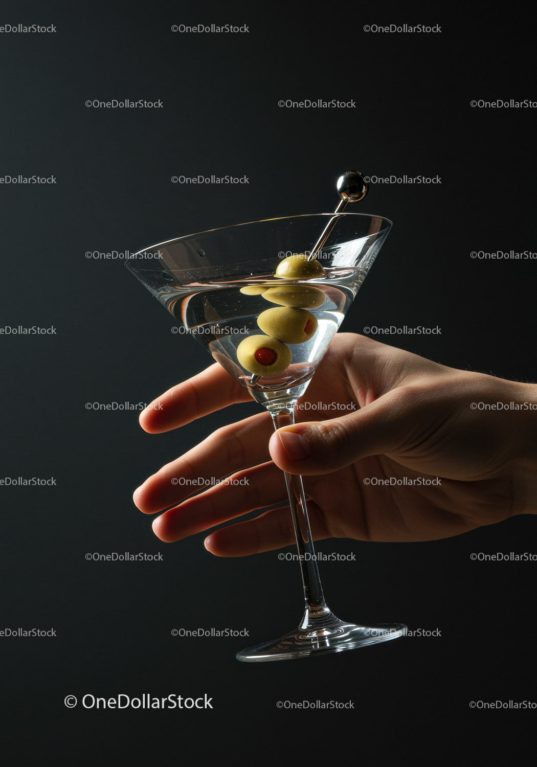 Dłoń trzymająca kieliszek Martini z zielonymi oliwkami na szpikulcu