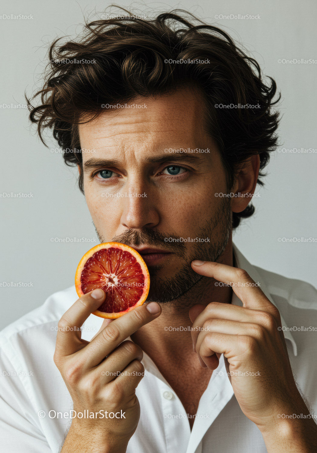 Elegant Man Holding Blood Orange Slice with Contemplative Expression