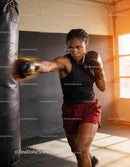 Focused female boxer training with punching bag indoors