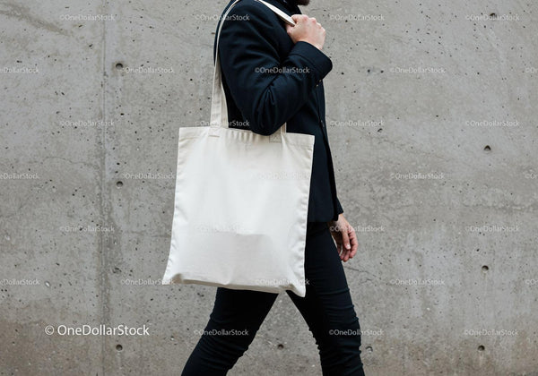 Man carrying blank white tote bag walking outdoors JPG Mockup Image