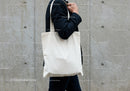 Person Carrying Blank Canvas Tote Bag Against Concrete Wall