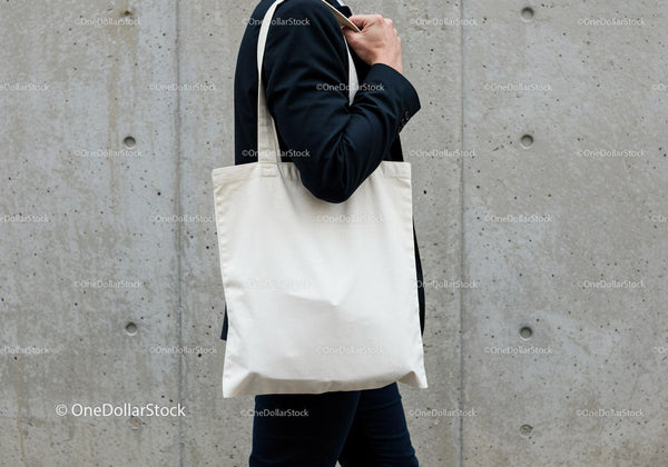 Person Carrying Blank Canvas Tote Bag Against Concrete Wall JPG Mockup Image