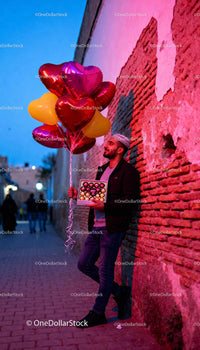 Man holding heart balloons and chocolates on street