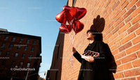 Young man holding heart balloons and chocolates outdoors