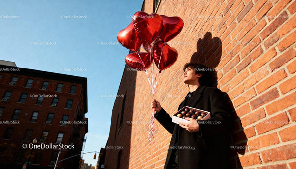Young man holding heart balloons and chocolates outdoors