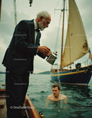 Elderly Man in Tuxedo Pouring Coffee on a Sailing Boat with Young Swimmer