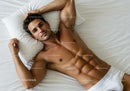 Relaxed muscular man lying on white bed resting