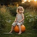 Toddler sitting on large pumpkin in garden at sunset