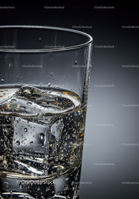 Clear glass of sparkling water with ice cubes closeup