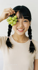 Young Woman with Braided Hair Enjoying Fresh Green Grapes in Bright Indoor Setting