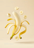 Peeled banana with floating slices on beige background