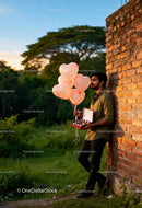 Man holding heart-shaped balloons and chocolates outdoors