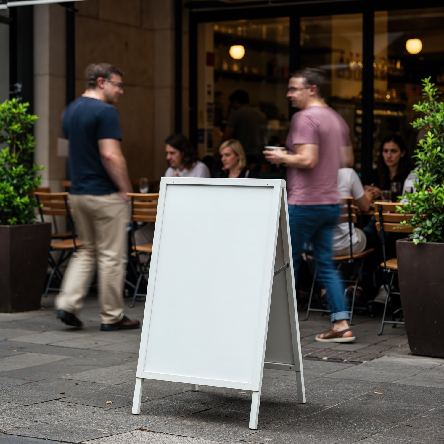 Blank sidewalk sign outside busy urban cafe