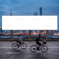 Cyclists Passing by Large Blank Billboard at Dusk