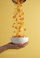 Cornflakes Falling Into White Bowl Held by Hand