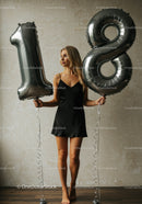 Young woman holding metallic 18 birthday balloons indoors