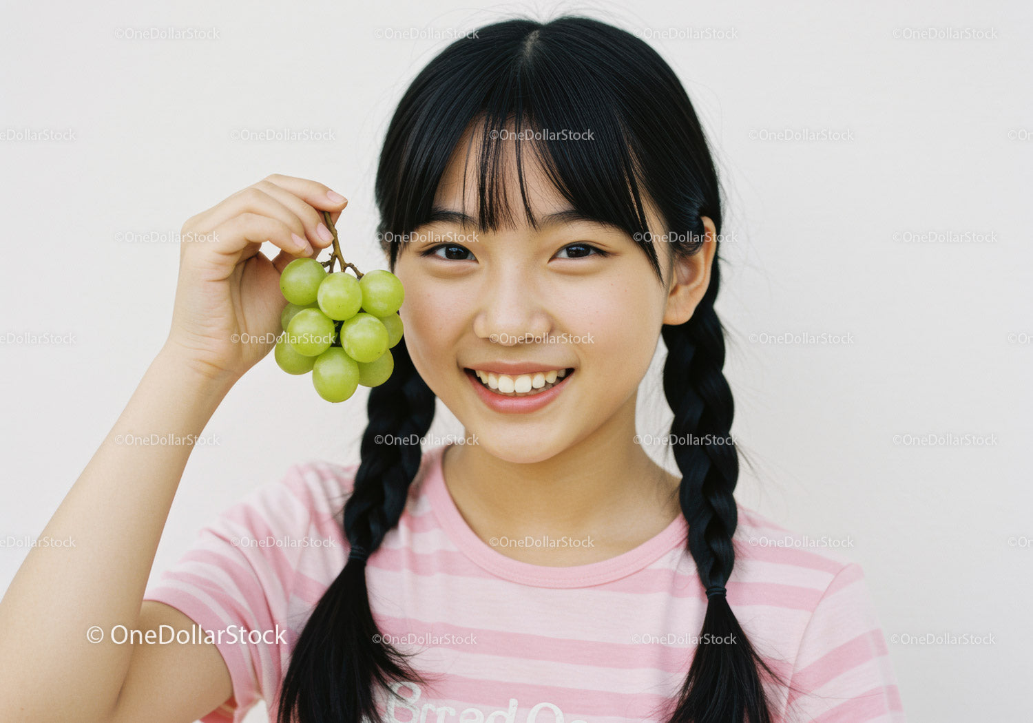 Smiling Girl with Pigtails Holding Green Grapes in Bright Indoor Setting