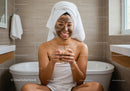 Happy Woman with Mud Face Mask Sitting in Bathtub in Bathroom