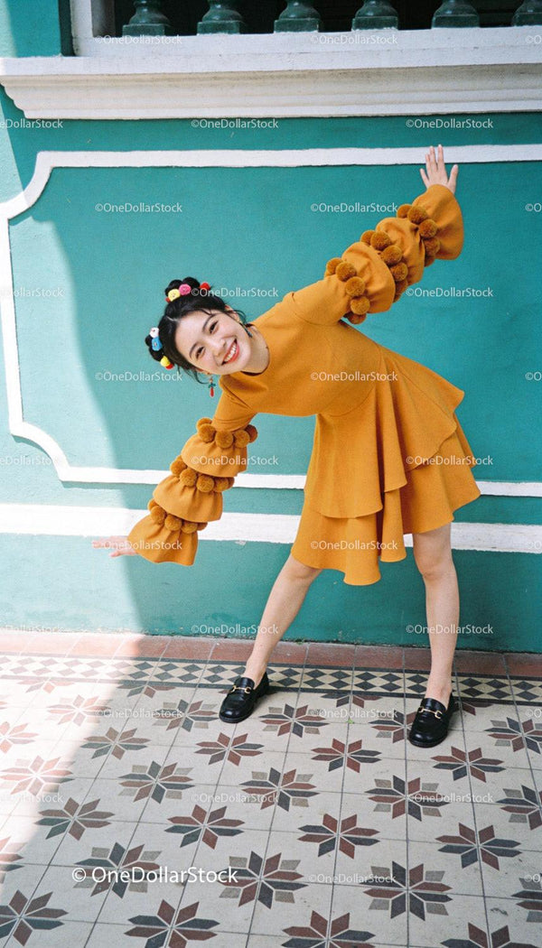 Joyful woman in mustard dress posing against turquoise wall
