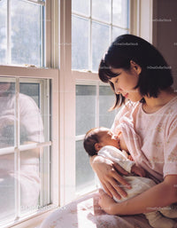 Mother tenderly breastfeeding newborn by sunlit window