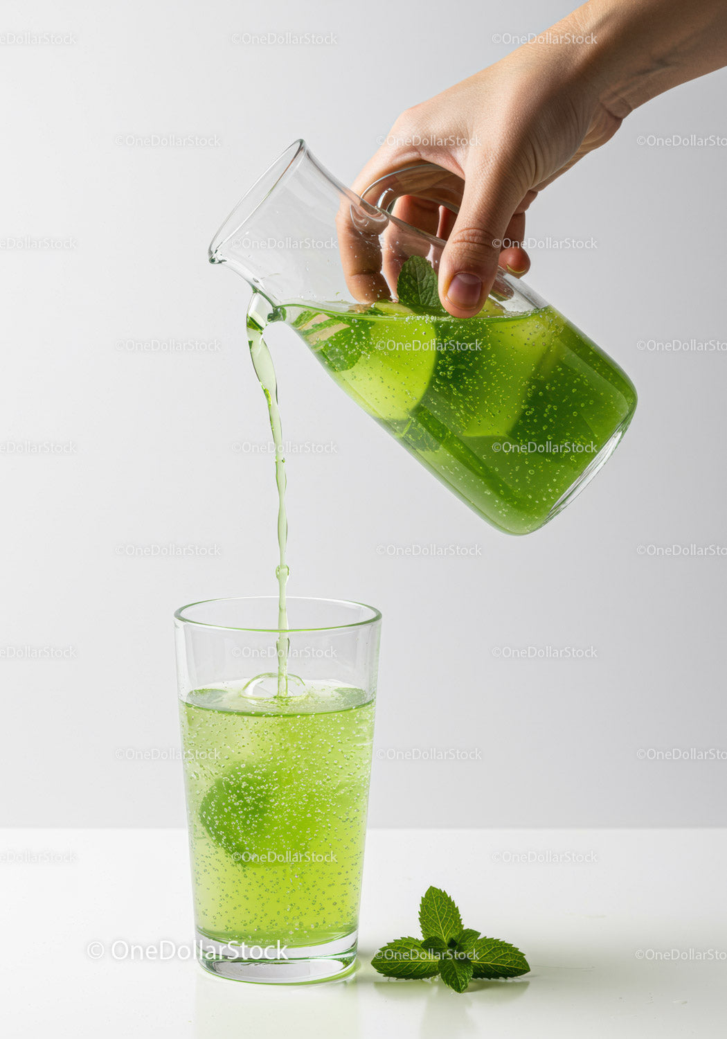 Hand pouring refreshing green mint lemonade into glass