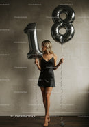 Young woman holding silver 18 number balloons indoors