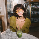 Stylish Young Woman with Yellow Glasses and Green Drink in Cafe