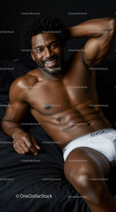 Smiling muscular man relaxing on black bed in white underwear