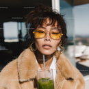 Fashionable woman with yellow glasses enjoying green juice outdoors