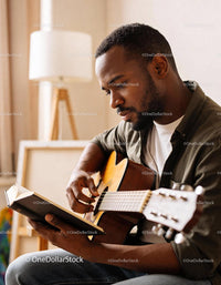 Focused man learning guitar chords with a book in cozy room