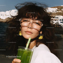 Young Woman Drinking Green Juice with Straw Near Sea and White Buildings