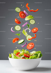 Fresh vegetable salad ingredients suspended above bowl