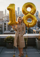 Young woman holding golden 18th birthday balloons outdoors