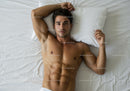 Athletic man relaxing on white bed with calm expression