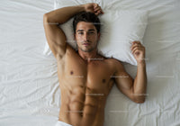 Athletic man relaxing on white bed with calm expression