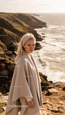 Woman in cozy beige cape on rocky coastline
