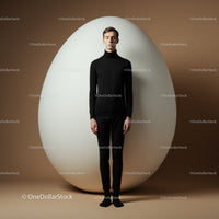 Serene young man standing still beside giant egg
