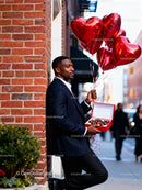 Man holding heart balloons and chocolates outdoors