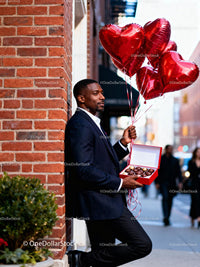 Man holding heart balloons and chocolates outdoors