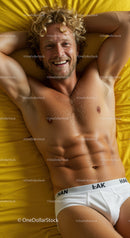 Smiling man relaxing on yellow bedding in white underwear