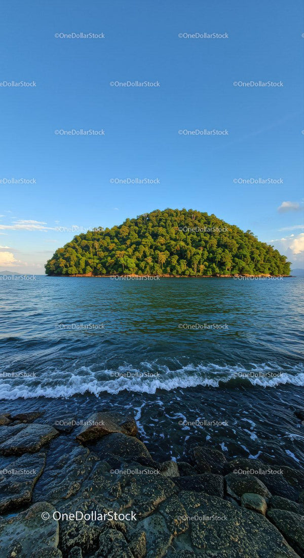 Tropical Green Island with Rocky Shoreline in Calm Blue Sea