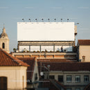 Large blank billboard over city rooftops at sunset