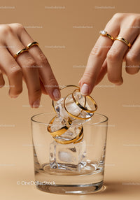 Hands Placing Gold Rings on Ice Cubes in Clear Glass