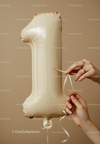 Hands tying ribbon on beige number one balloon
