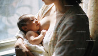 Mother lovingly breastfeeding newborn baby near window