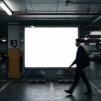 Blurred man walking past illuminated billboard in parking garage